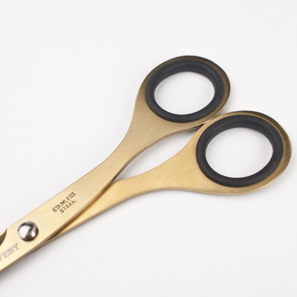 Gold-colored stainless steel scissors with black rubber lined loops and 'TOOLS to LIVEBY' branding on blades on a light background.