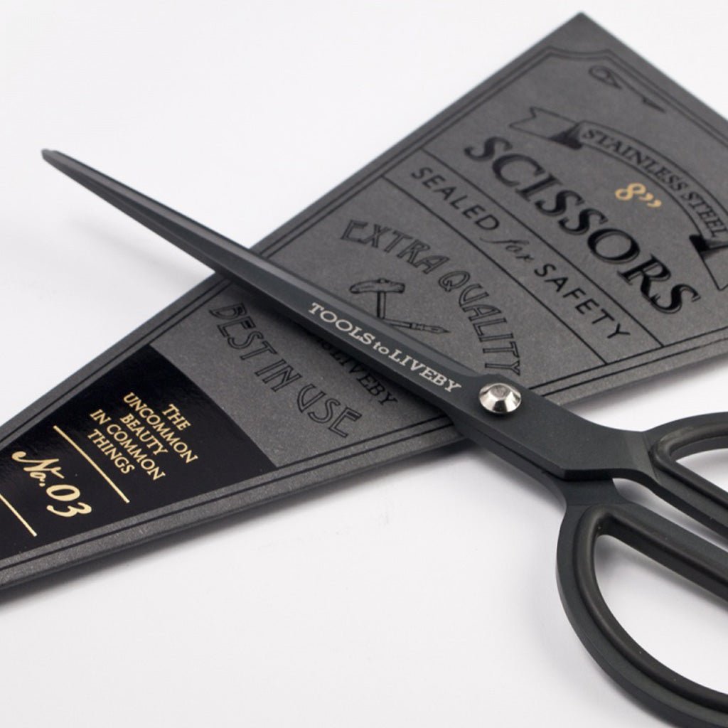Matte black scissors with rounded handles next to black packaging on white surface
