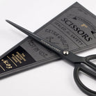 Matte black scissors with rounded handles next to black packaging on white surface