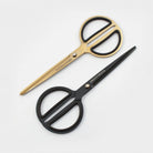 Gold-toned scissors with black rubberized finger loops and matte black scissors with rounded handles on white background
