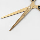 Gold-colored scissors with black handles and a silver pivot screw, featuring the text 'TOOLS TO LIVEBY' printed on one blade, set against a plain light gray background.