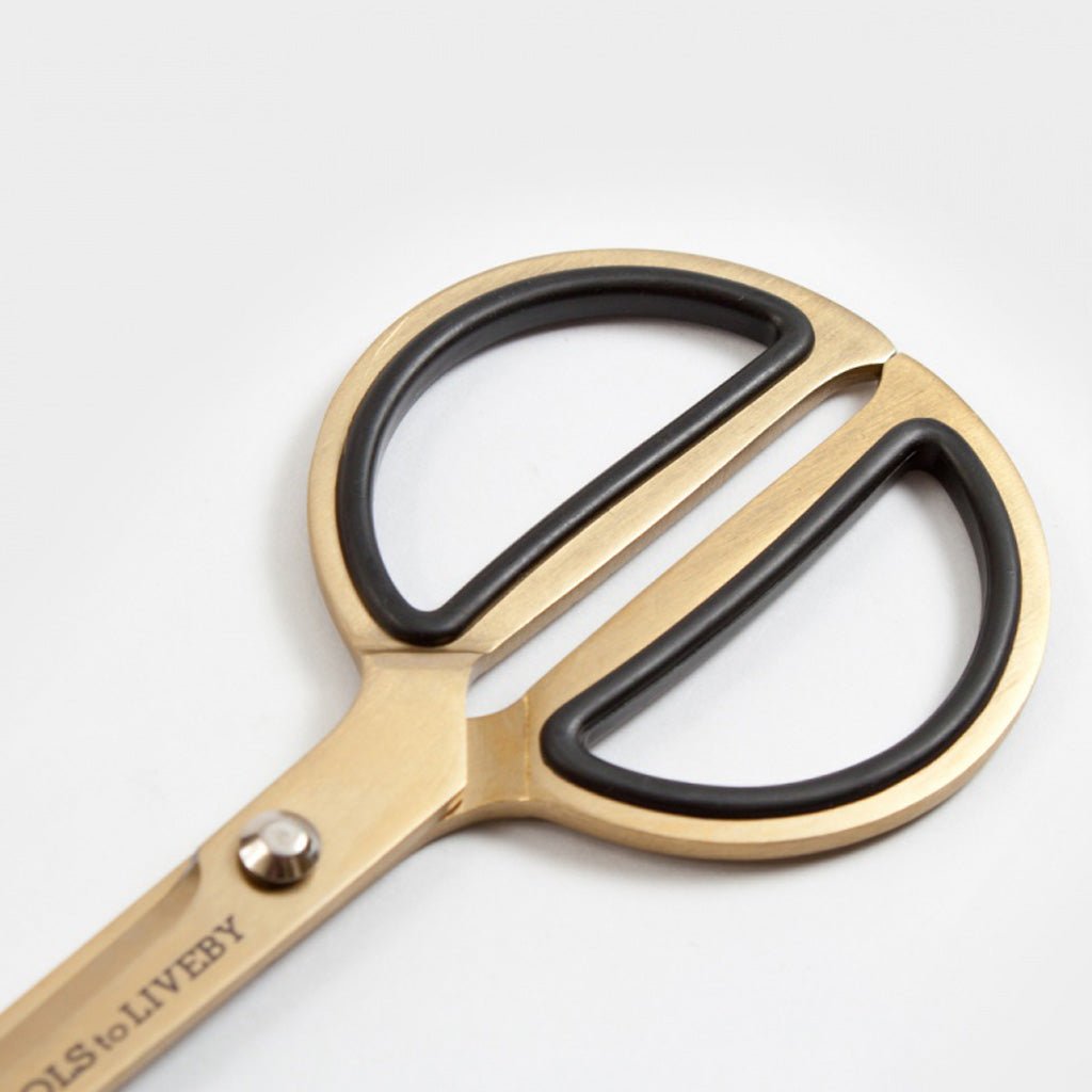Gold-toned scissors with black rubberized finger loops and a visible 'TOOLS to LIVE BY' brand engraving on the handle, photographed on a clean white background.