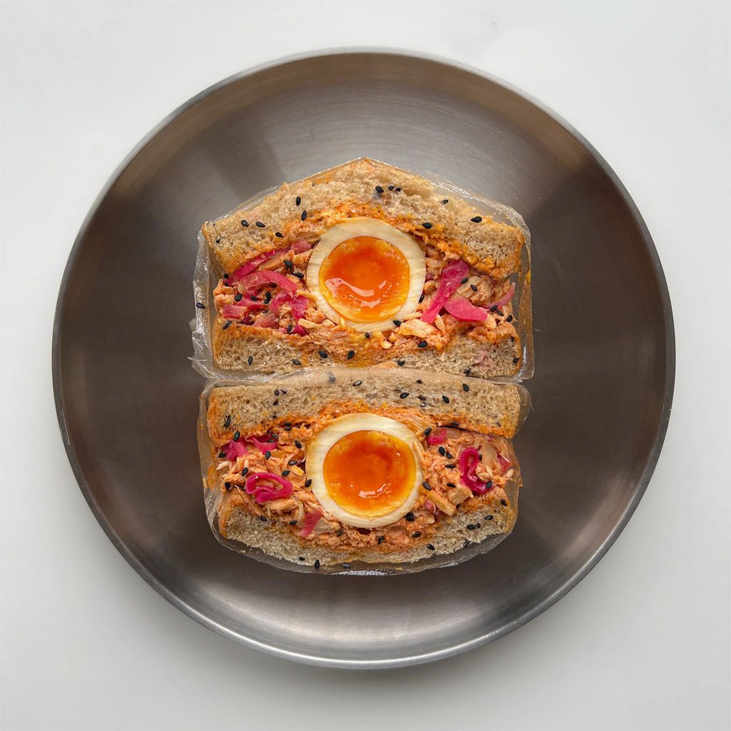 Two sandwiches with boiled eggs, tuna, and pickled onions on a metal plate.