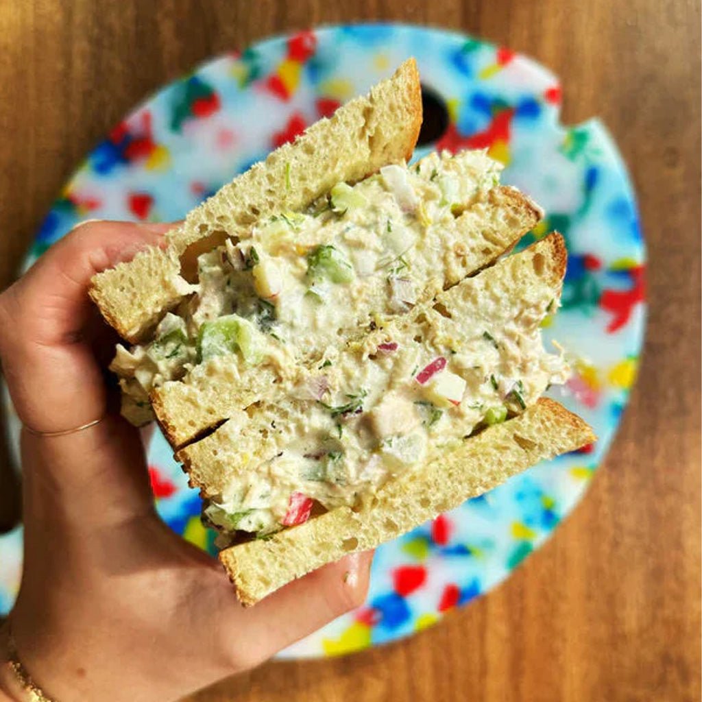 Hand holding tuna fish sandwich over colorful plate on wooden surface