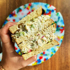 Hand holding tuna fish sandwich over colorful plate on wooden surface