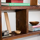 Wooden shelf with books, a bowl, and other objects on a white wall background