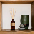Aromatherapy diffuser with reeds and a green ceramic vase on a wooden shelf.