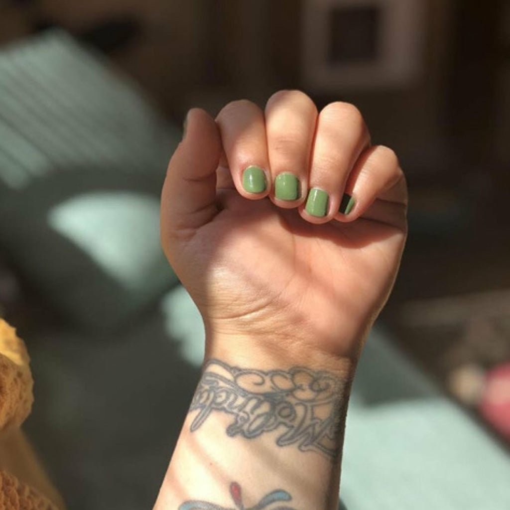 Hand with green nail polish and tattoos on a blurred background
