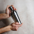 Person holding a silver cocktail shaker against a neutral background