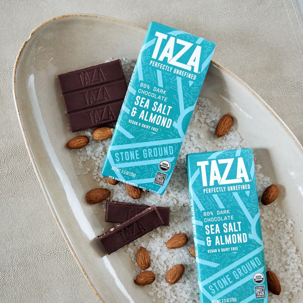 Taza chocolate bars and packaging on a textured surface with sea salt and almonds.