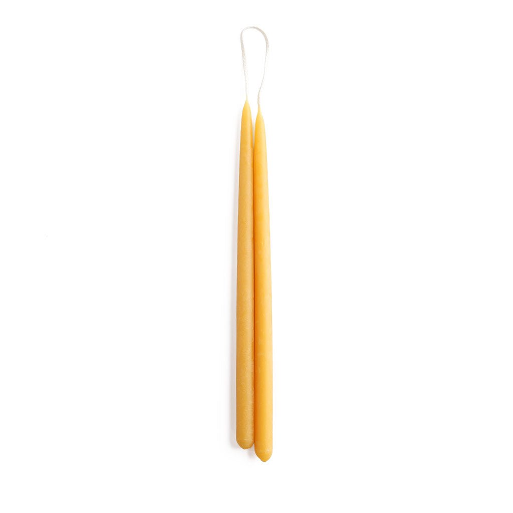 A set of two thin yellow beeswax taper candles on white background