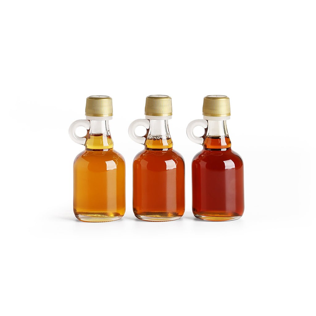 Three small glass bottles of golden, amber, and dark New England Maple Syrup