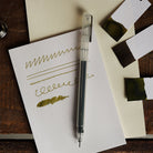 Pen on a piece of paper with green writing on a wooden surface
