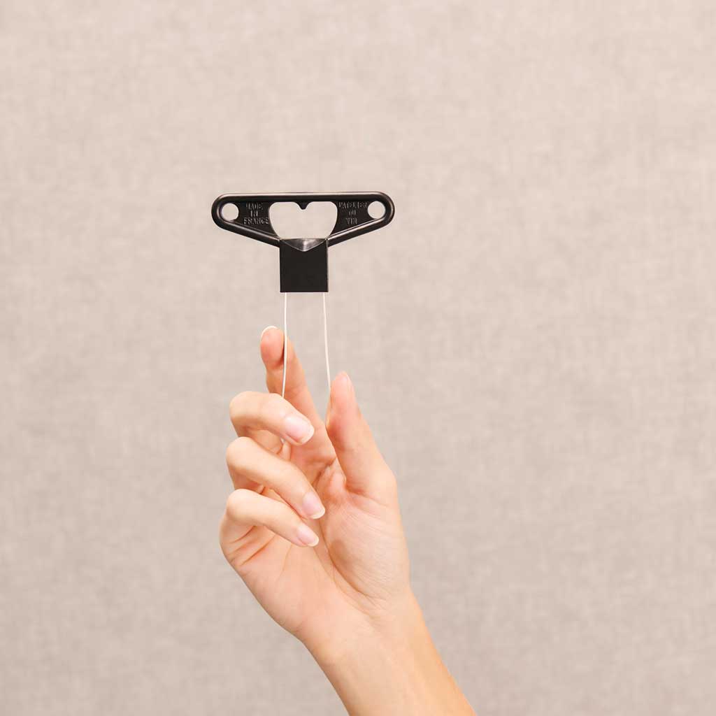 Hand holding a black cork extractor tool against a beige background