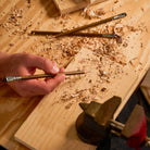 A lifestyle photo showing a hand holding the Blackwing Volumes 21 pencil on a wooden workspace with wood shavings scattered on it. 