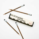 A box of Blackwing Volumes 21 pencils on a white background. Four pencils lay outside the box. They are dark brown with silver ferrules and black erasers. 