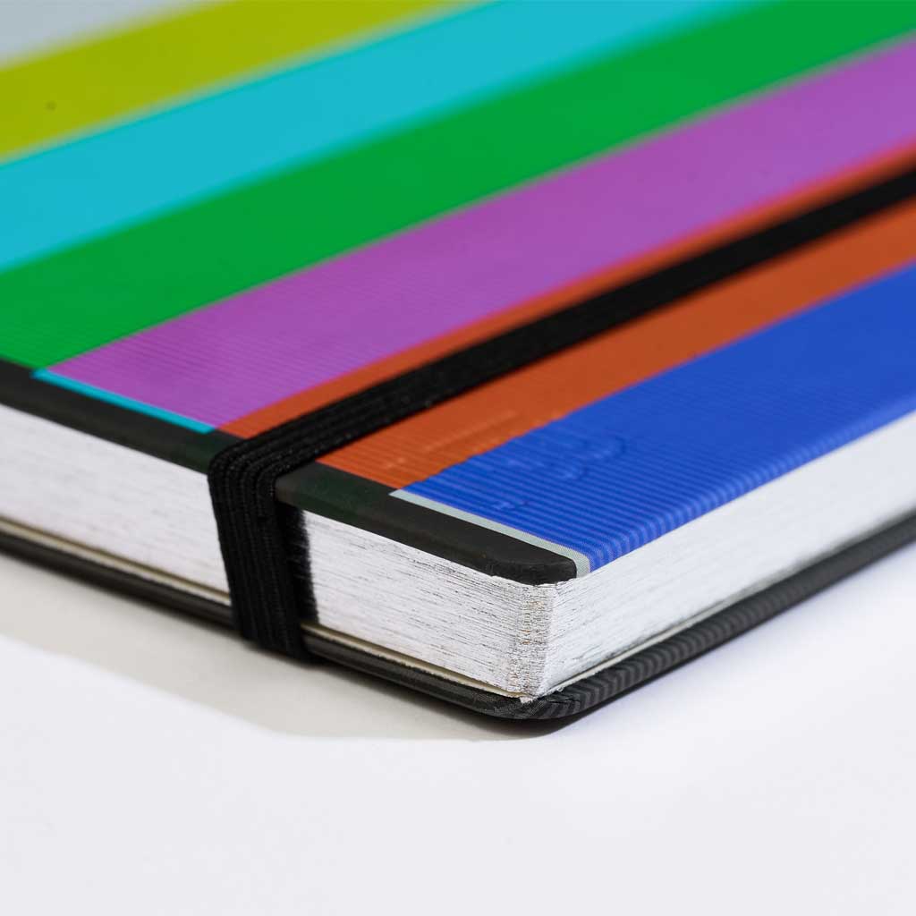 Colorful notebook with a black elastic band and silver gilded edged pages on a white background