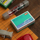 MAX Remover eraser in turquoise packaging, surrounded by correction tape and stationery supplies on an orange folder.
