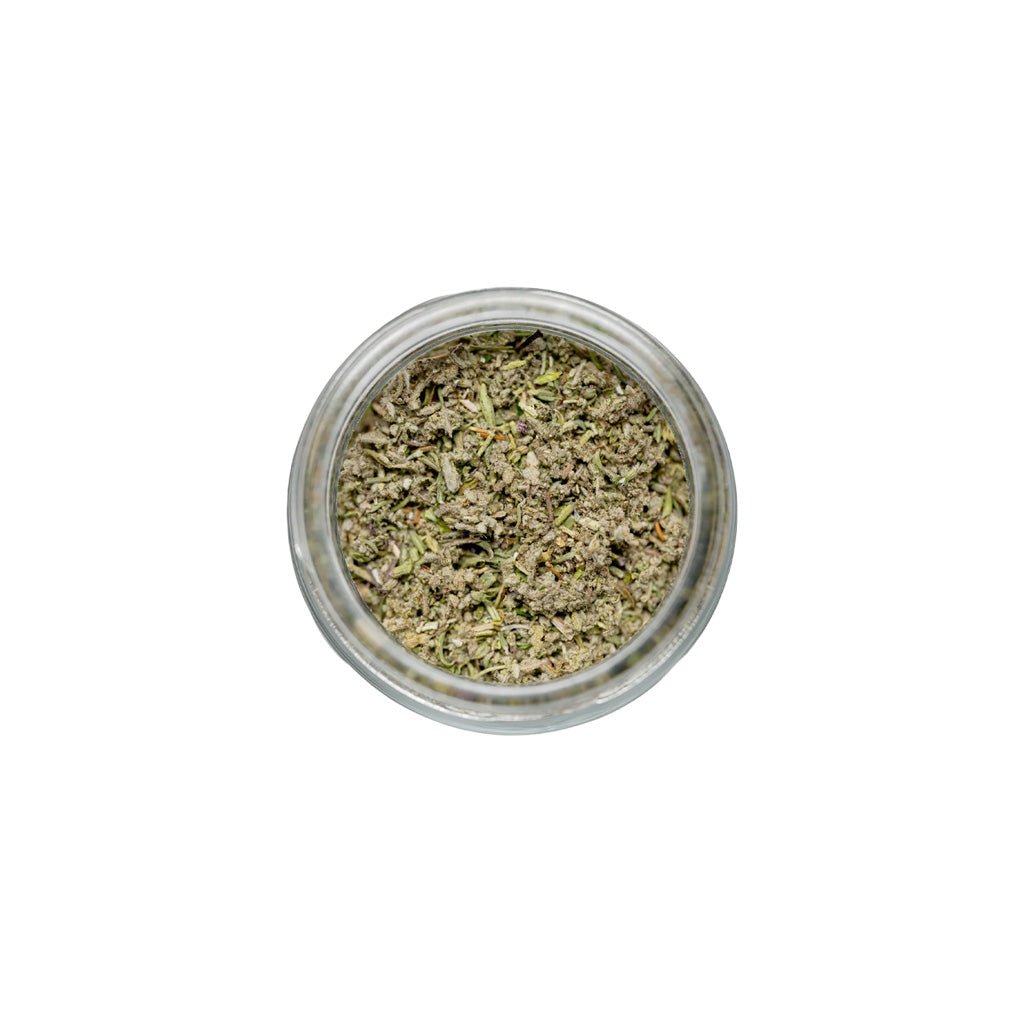 Small glass jar filled with dried herbs on a white background