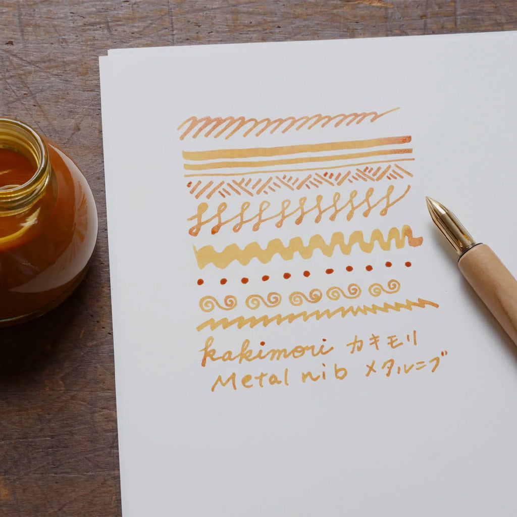 Kakimori brass nib in wooden dip pen with writing example in orange ink on white paper