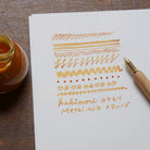 Kakimori brass nib in wooden dip pen with writing example in orange ink on white paper