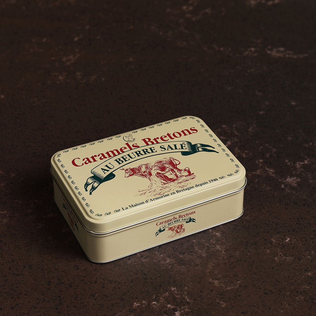 A cream colored tin with illustrations of cows in red with green lettering.