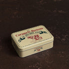 A cream colored tin with illustrations of cows in red with green lettering.