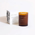 An amber glass jar candle labeled APPLE CIDER next to its white packaging box with a black botanical illustration, set against a clean white background.