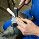 Person working on a rivet in a wooden knife handle with a hammer and vise