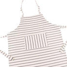 A white cotton apron for children with thin horizontal stripes, featuring a central vertical-striped pocket and hip ties and neck loop, shown on a plain white background.