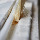 A close-up shot of a natural cleaning brush with light tan bristles, positioned inside the groove of a white textured wall or siding.