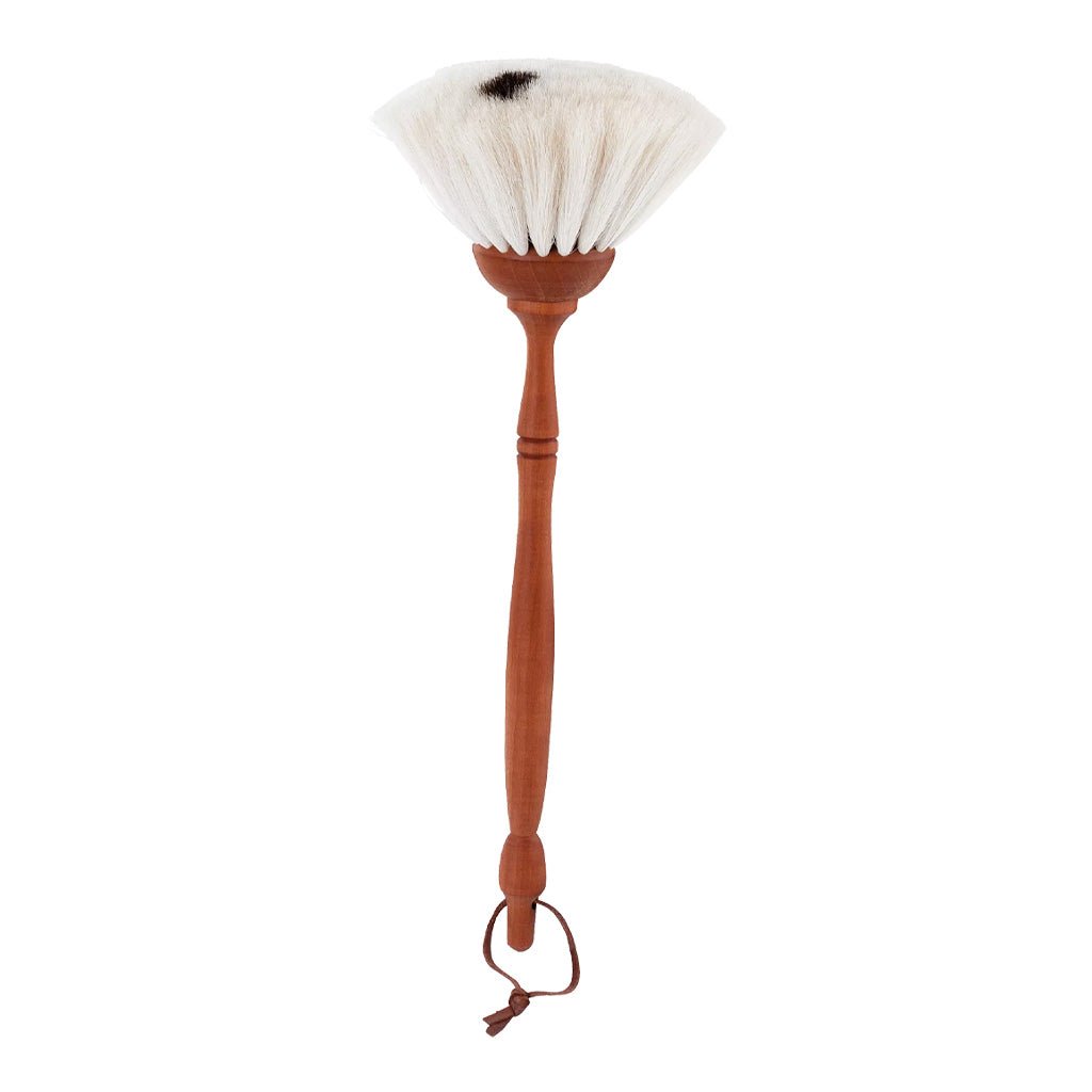 A goat hair dust brush with a pear wood handle and leather loop and white bristles on white background