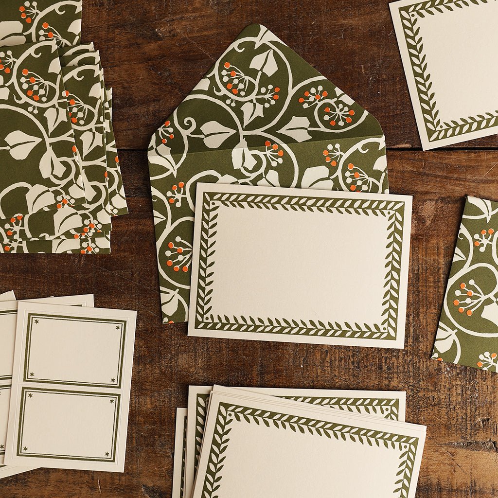 Green Ivy Notecard and Envelope Set arranged on a wooden table, featuring botanical envelopes, bordered cards, and labels.