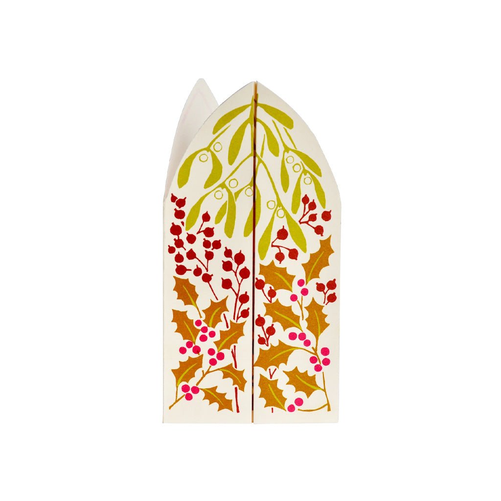 A festive paper greeting card featuring mistletoe, holly leaves, and berries closed on a white background.