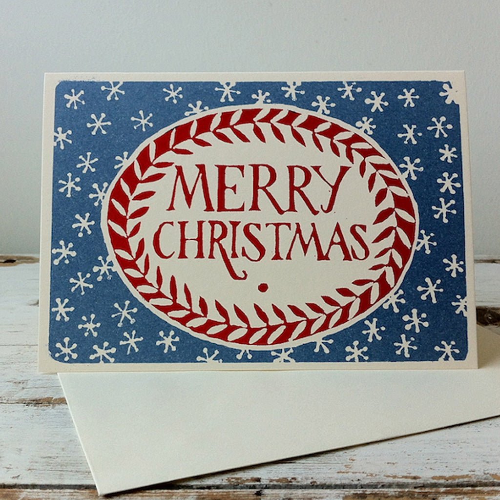 Red and blue Merry Christmas card standing upright on top of envelope.