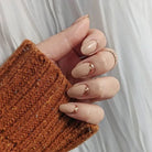 Hand wearing neutral nail polish with glittery candied ginger accents against light background