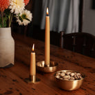 Natural taper candles lit in brass holders, next to bowl of nuts on table.