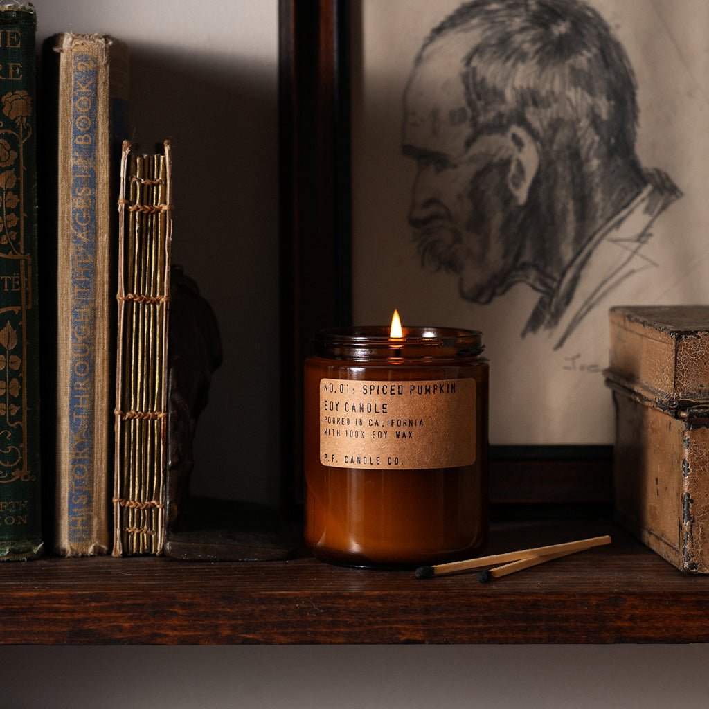 A lit Spiced Pumpkin candle on a shelf next to books.