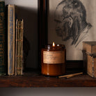 A lit Spiced Pumpkin candle on a shelf next to books.