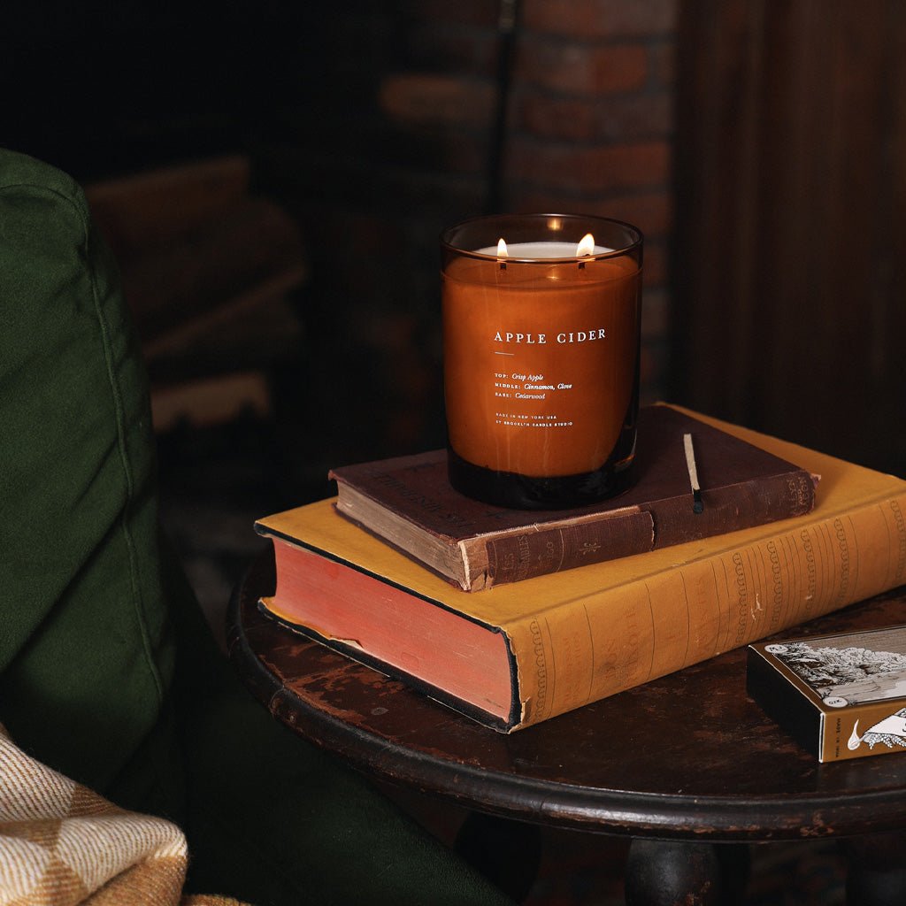 A lit Apple Cider candle on a stack of books.