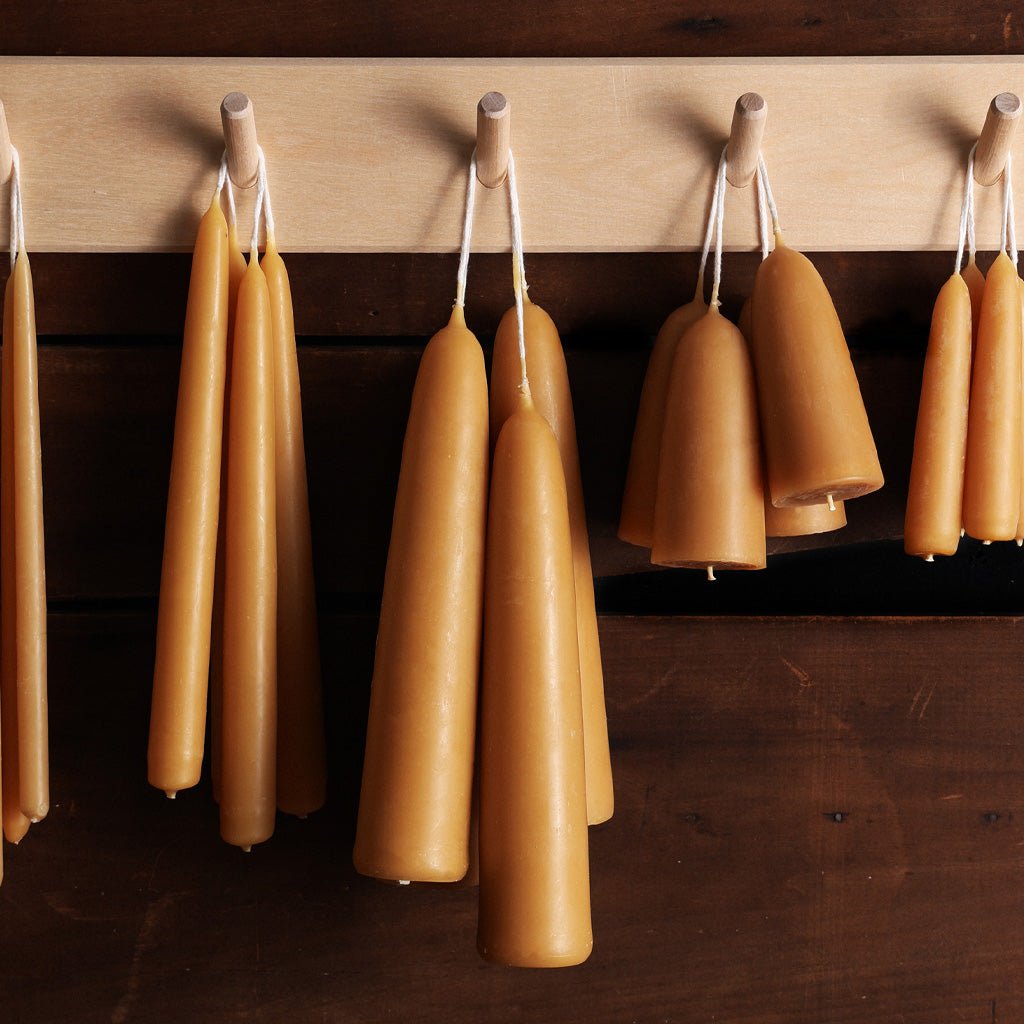 Natural-colored taper candles in various sizes on wooden peg rack.