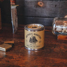 Captain's Quarters candle tin on a wooden surface with vintage items in the background