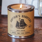 Candle in a tin labeled 'Captain's Quarters' on a wooden surface