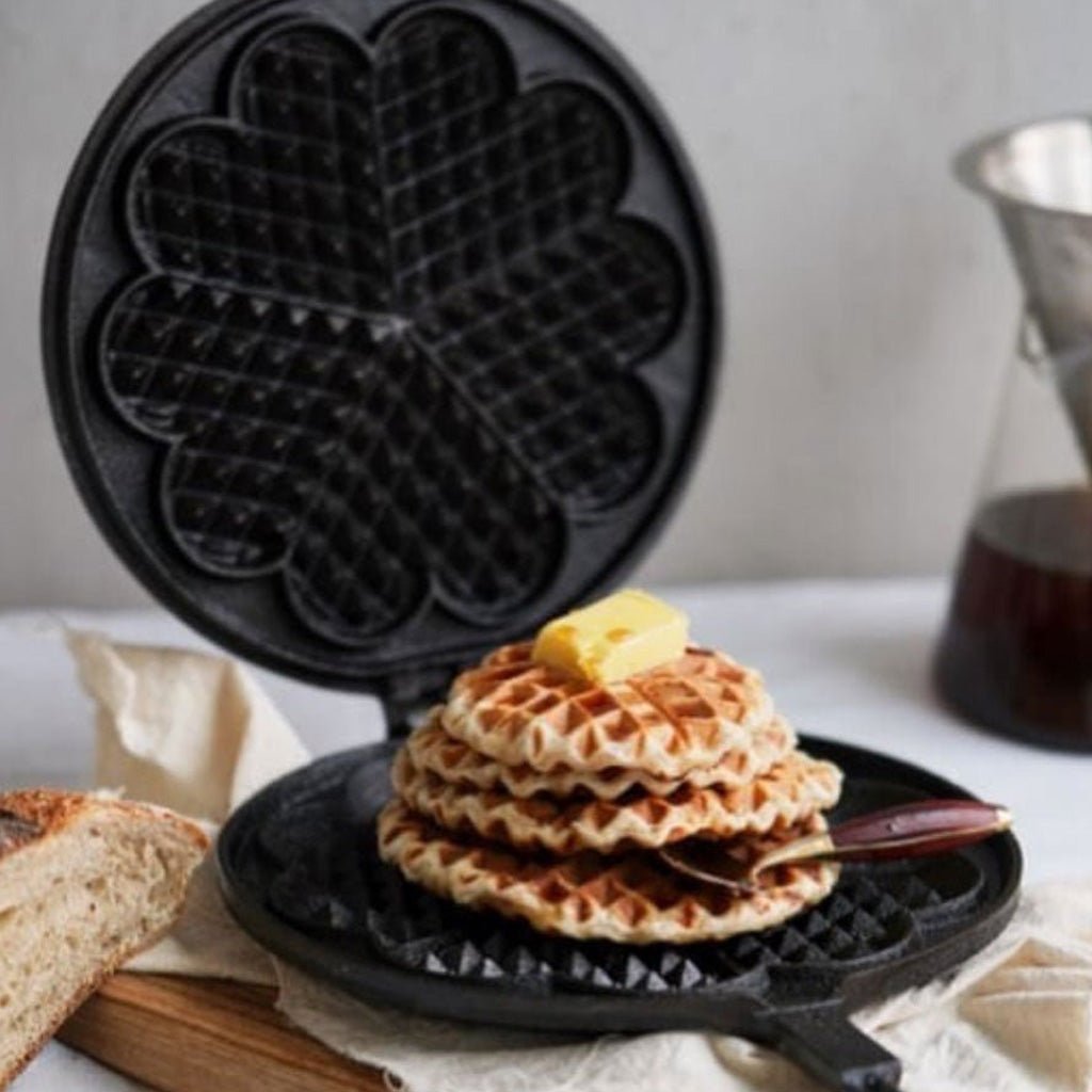 Cast iron waffle iron with stack of cooked waffles on breakfast table