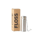 Charcoal floss in stainless steel holder next to kraft box packaging on white background