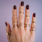 Hand wearing dark red cherry pie nail polish with gold rings against purple background
