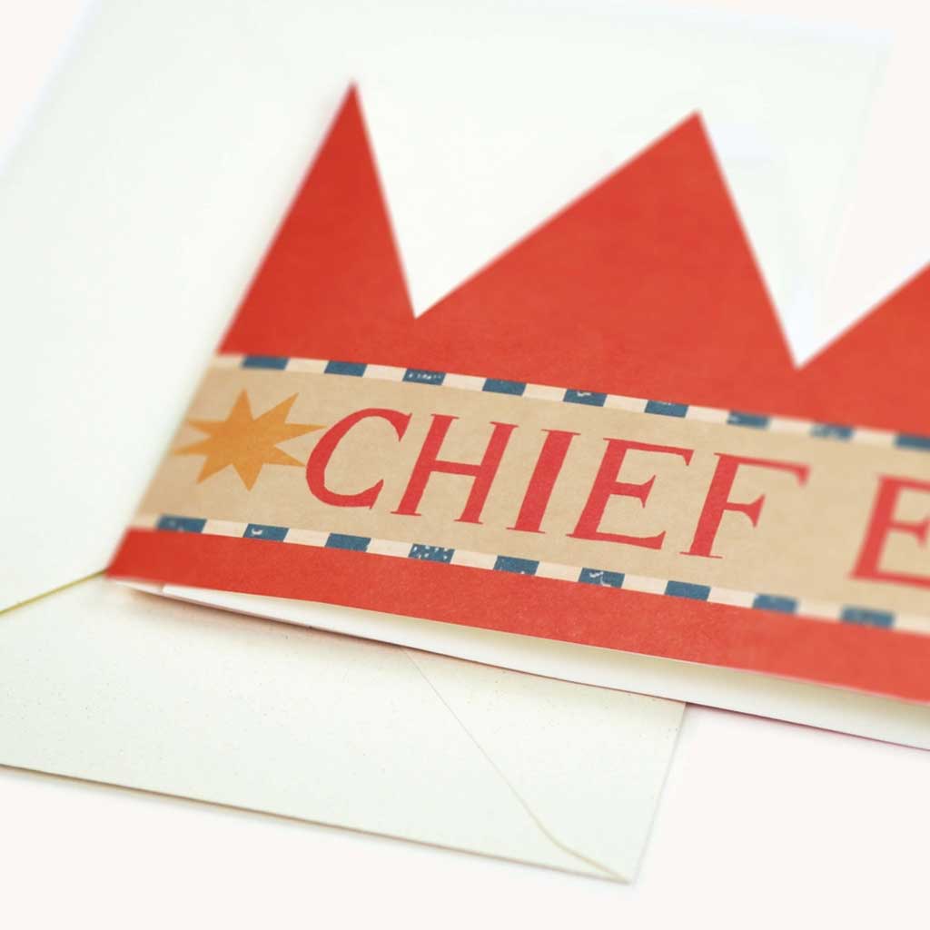 Close up of party hat card with red brim and 'CHIEF' text on a white background