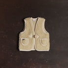 A small children's woolen vest in a natural cream color on a dark background.