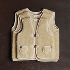 Three cream-colored woolen vests stacked one on top of the other on a dark background.