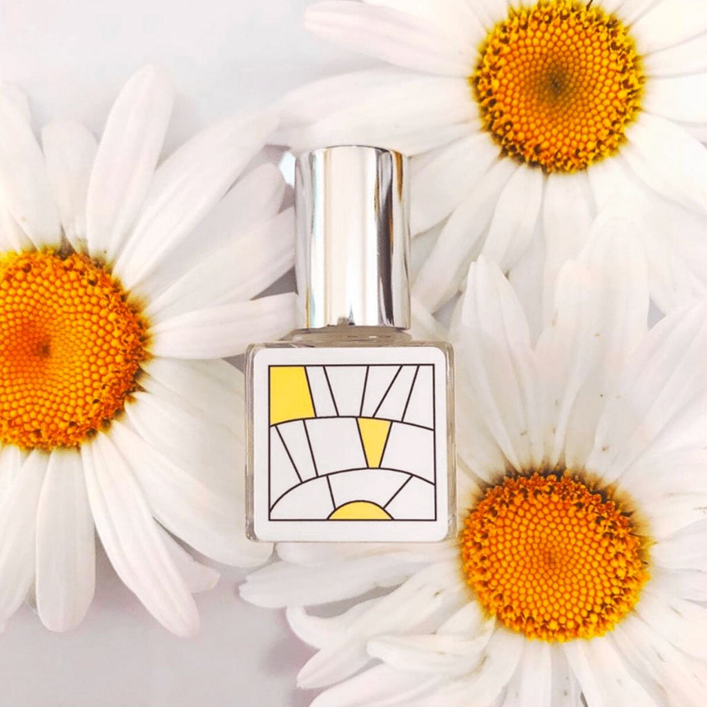 Bottle of citrus perfume oil resting among daisies 